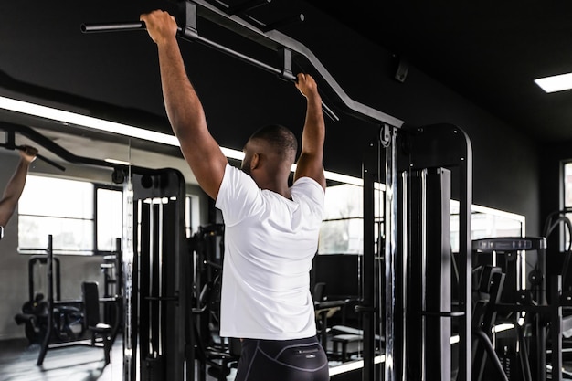 Homem africano em forma e musculoso puxando na barra horizontal em uma academia