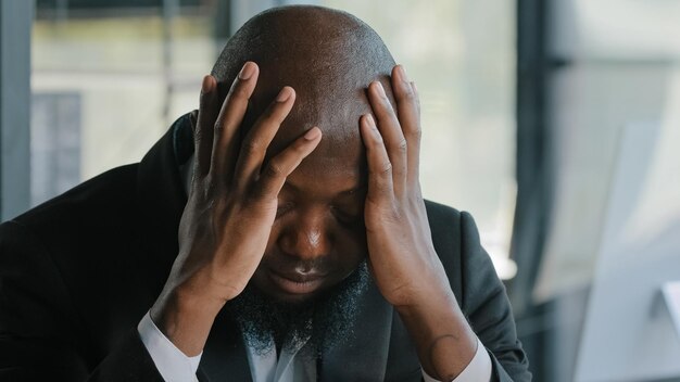 Homem africano exausto e doente sofre de síndrome de enxaqueca com dor de cabeça, segure a cabeça pelas mãos cansadas