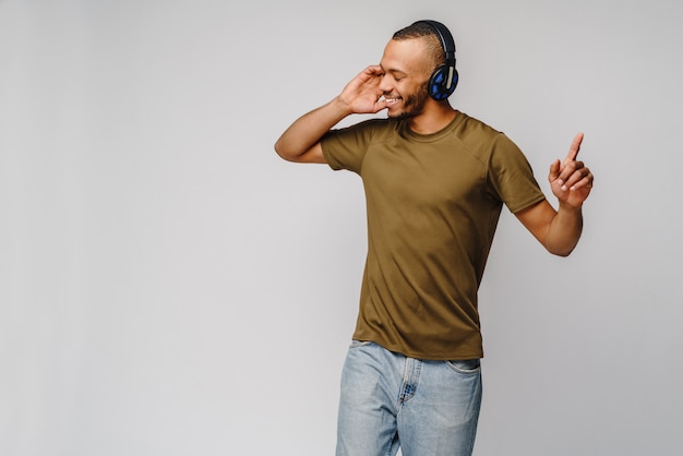 Homem africano feliz sorrindo ouvindo música em fones de ouvido na parede cinza
