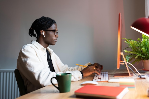 Homem africano focado desenvolvedor web freelancer escrevendo código usando computador sentado no escritório em casa