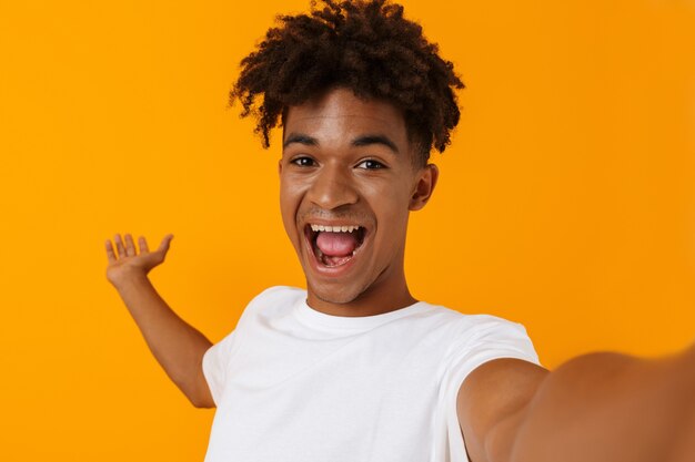 Homem africano jovem feliz posando isolado sobre o espaço amarelo, mostrando copyspace make se; fie pela câmera.