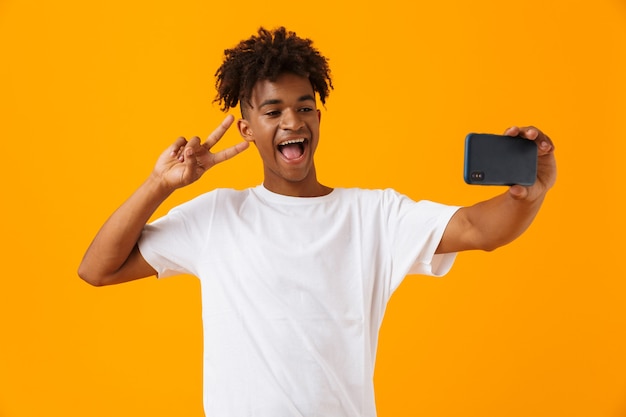 Homem africano posar isolado sobre o espaço amarelo, tirar uma selfie por telefone.