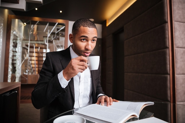 Foto homem africano sério sentado à mesa com o diário e bebendo café no hotel