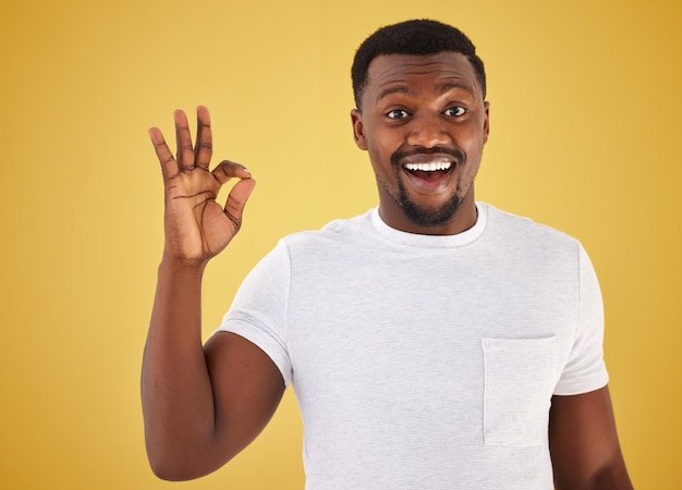 Homem africano sinal ok e retrato de estúdio para sorriso uau e surpresa para votação de revisão ou como por mão de pessoa de fundo amarelo e emoji para escolha de feedback ou decisão com símbolo de ícone e feliz