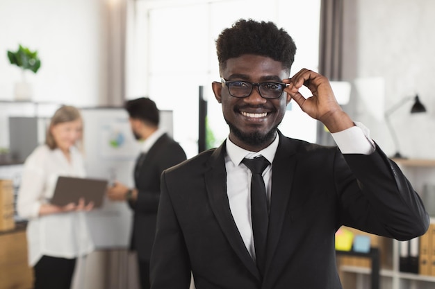 Homem africano sorridente de terno e óculos posando no escritório