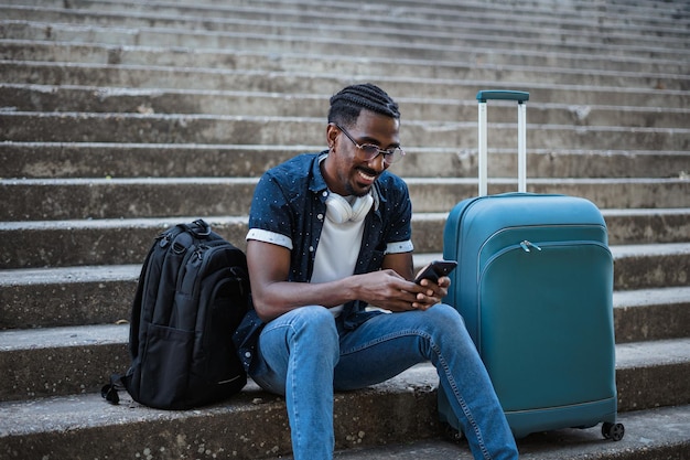 Homem africano usando seu telefone enquanto está sentado nas escadas Ele está esperando o trem chegar