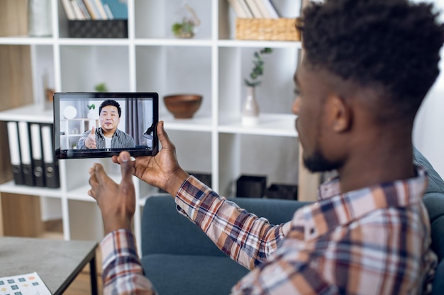 Homem africano usando tablet para videochamada com colega de trabalho asiático