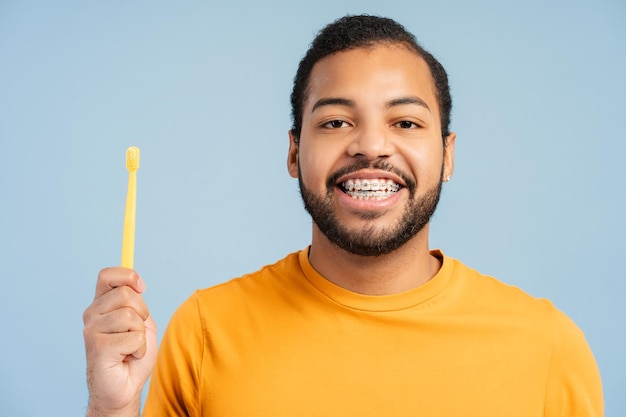 Homem afro-americano alegre com aparelhos ortopédicos segurando uma escova de dentes e olhando para a câmera