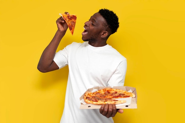 Foto homem afro-americano alegre em camisa branca segura uma caixa de pizza em fundo isolado amarelo