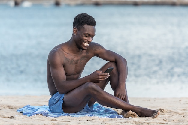 Homem afro-americano alegre usando smartphone na praia