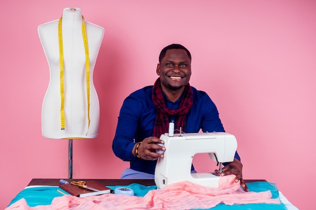 Homem afro-americano alfaiate costureira oficina estilista modelo masculino designer de roupas o processo de criação de uma nova coleção de vestidos em fundo rosa no estúdio copyspace