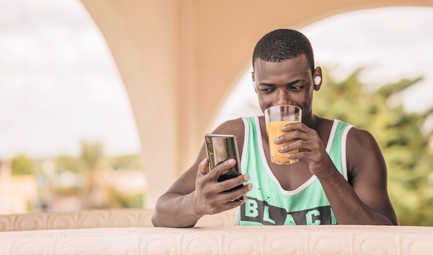 Homem afro-americano bebendo suco e usando celular