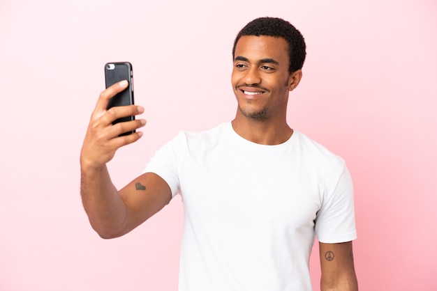 Homem afro-americano bonito em fundo rosa isolado fazendo uma selfie com o celular