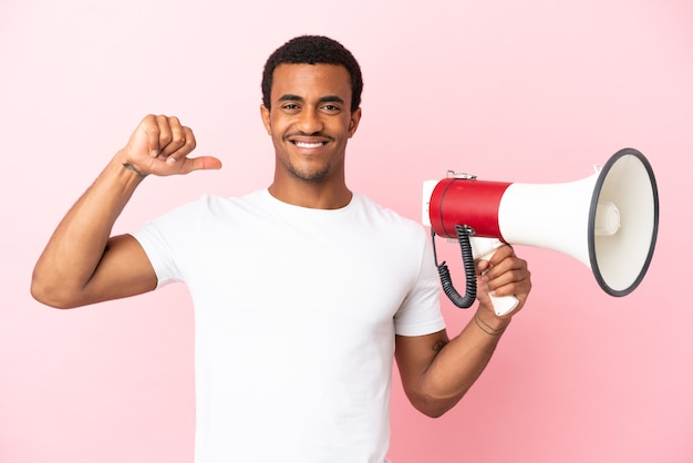 Homem afro-americano bonito em um fundo rosa isolado, segurando um megafone, orgulhoso e satisfeito consigo mesmo