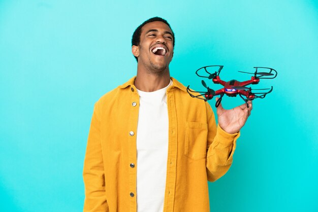 Homem afro-americano bonito segurando um drone sobre um fundo azul isolado rindo