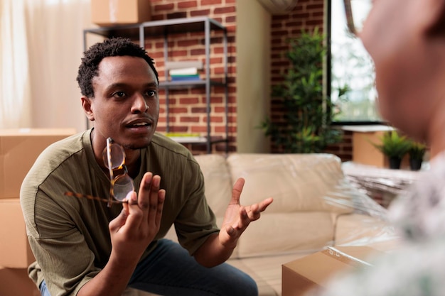 Homem afro-americano brigando com a esposa por realocação de propriedade, discutindo e discordando das ideias de decoração. discutir e sentir-se frustrado por morarem juntos.