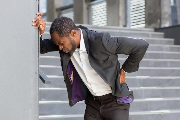 Homem afro-americano cansado e doente do lado de fora do prédio de escritórios tem forte dor nas costas empresário