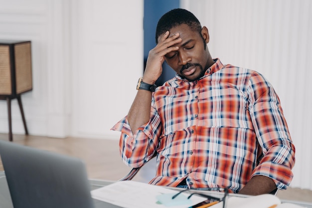 Homem afro-americano cansado sofre de dor de cabeça no laptop pensando em problemas de negócios estresse no trabalho