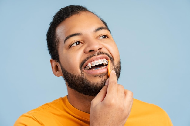 Homem afro-americano com aparelhos ortodônticos usando fio dental fácil para limpar dentes olhando para longe