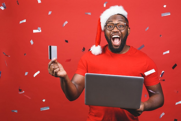 Homem afro-americano com chapéu de Papai Noel segurando laptop