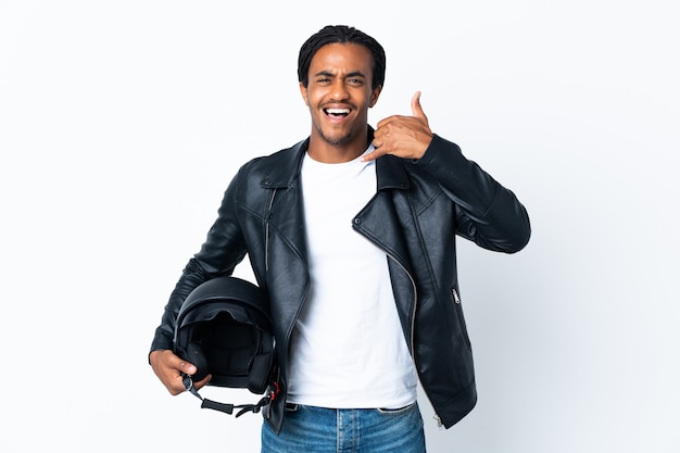 Homem afro-americano com tranças, segurando um capacete de motocicleta, isolado no fundo branco, fazendo gesto de telefone. Ligue-me de volta sinal