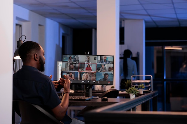 Homem afro-americano conversando com colegas de trabalho em videoconferência remota, usando reunião de teleconferência on-line para discutir sobre negócios. Conversando na videochamada da internet com a webcam à noite.