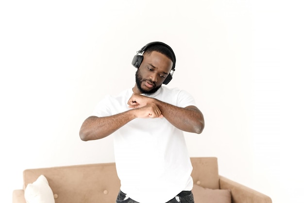 Homem afro-americano curtindo música em fones de ouvido grandes sem fio e dançando em casa relaxe sozinho