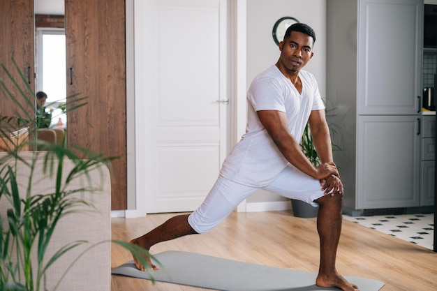 Homem afro-americano de ajuste muscular fazendo exercício de fitness esportivo em pé no tapete de ioga