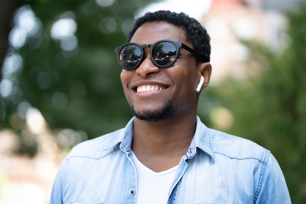 Homem afro-americano de óculos escuros e sorrindo em pé ao ar livre no parque.