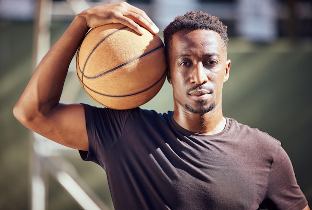 Homem afro-americano de retrato em pé com uma bola de basquete na quadra Atleta masculino fitness ou jogador segurando uma bola esportiva depois de jogar treinamento e praticar jogo em segundo plano em uma quadra