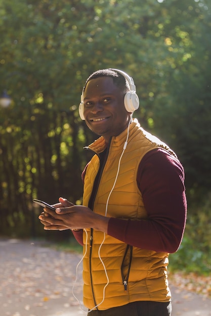 Homem afro-americano de retrato ouve música no fundo do parque de outono Gadget app e conceito de serviço de streaming