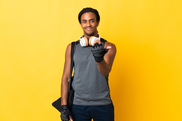 Homem afro-americano do esporte jovem com tranças com bolsa isolada no fundo amarelo, convidando para vir com a mão. Feliz que você veio