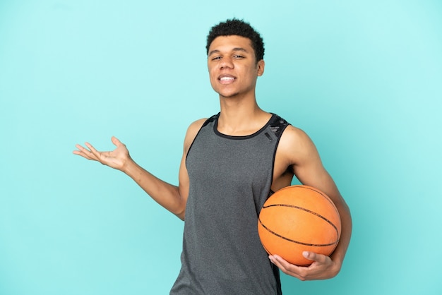 Homem afro-americano do jogador de basquete isolado em um fundo azul, estendendo as mãos para o lado para convidar para vir