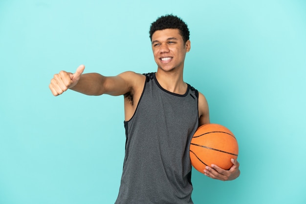 Homem afro-americano do jogador de basquete isolado em um fundo azul fazendo um gesto de polegar para cima