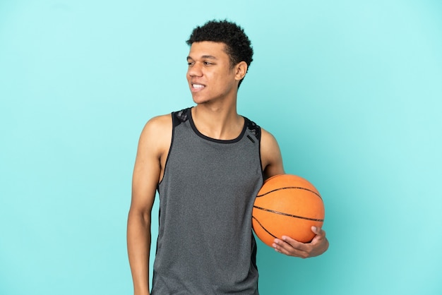 Homem afro-americano do jogador de basquete isolado em um fundo azul, olhando para o lado e sorrindo