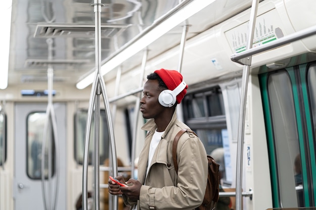 Homem afro-americano do milênio no metrô, usando telefone celular, ouve música com fones de ouvido sem fio no transporte