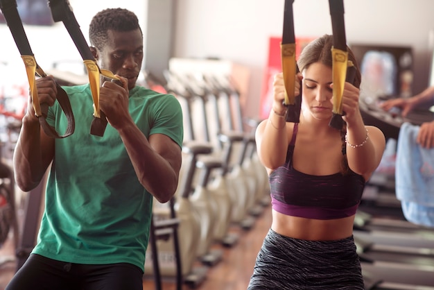 Homem afro-americano e jovem mulher fazendo exercícios trx