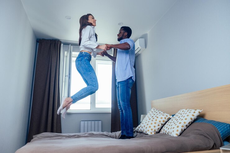 Foto homem afro-americano e mulher asiática pulando na cama segurando as mãos um do outro