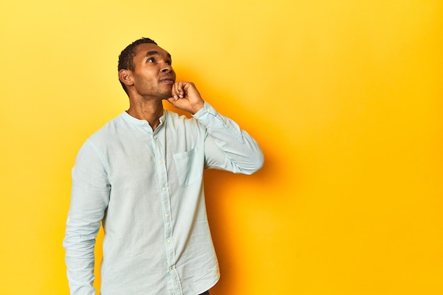 Homem afro-americano em camisa azul estúdio amarelo olhando de lado com dúvidas