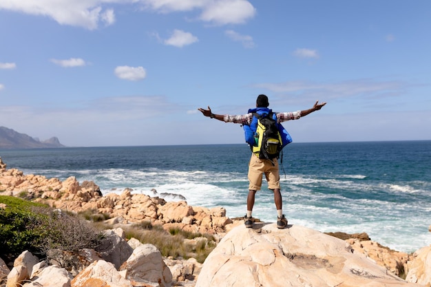 Homem afro-americano em forma usando mochila caminhando espalhando os braços na costa. estilo de vida saudável, exercitando-se na natureza.