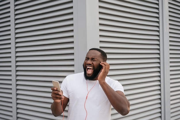 Homem afro-americano emocional ouvindo música ao ar livre cantando