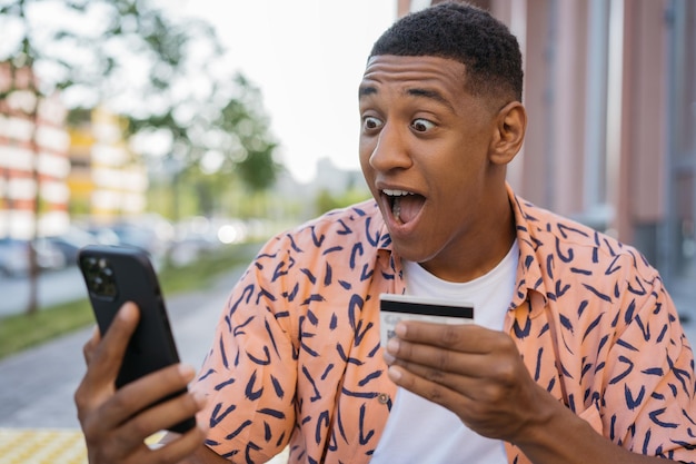 Homem afro-americano espantado com cartão de crédito, comprando online com promoções