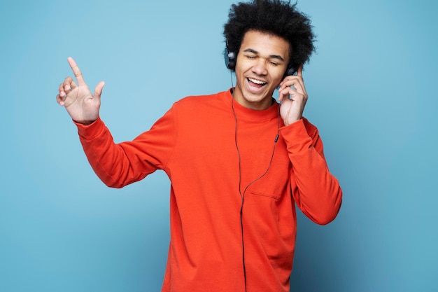 Homem afro-americano estiloso e emocional usando fones de ouvido ouvindo música, cantando, dançando