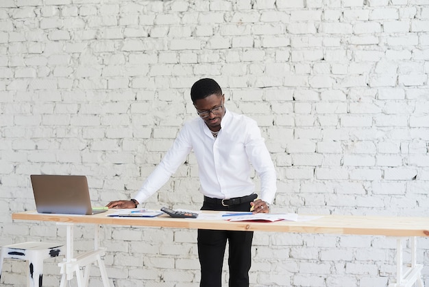 Homem afro-americano feliz e focado, fazendo uma videochamada com parceiros clientes. Jovem negro usa laptop em um escritório moderno.