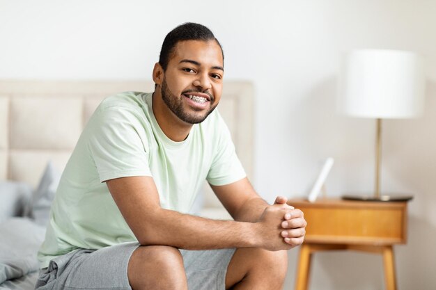 Homem afro-americano feliz sentado na cama com um tablet