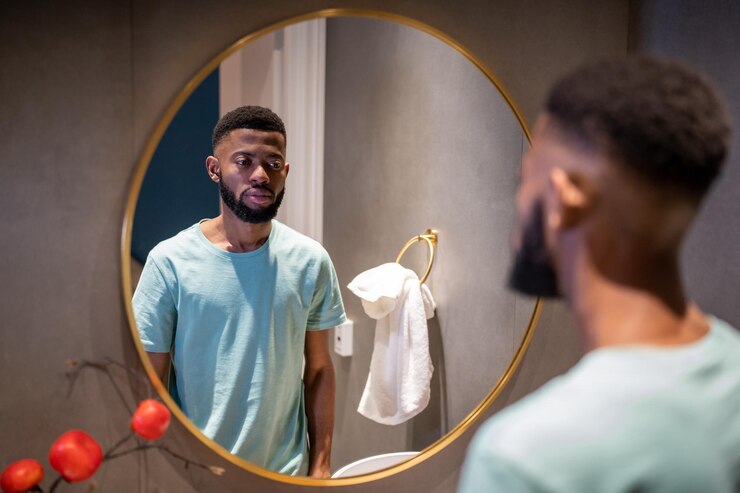 Foto homem afro-americano infeliz olhando para o espelho na casa de banho sentindo-se insatisfeito com sua aparência