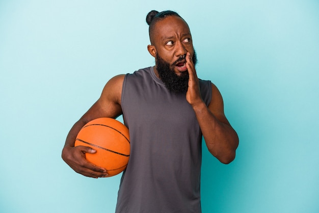 Homem afro-americano jogando basquete isolado na parede azul está contando uma notícia secreta sobre a travagem e olhando para o lado