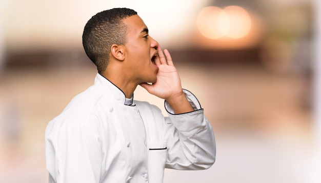 Homem afro-americano jovem chef gritando com a boca aberta