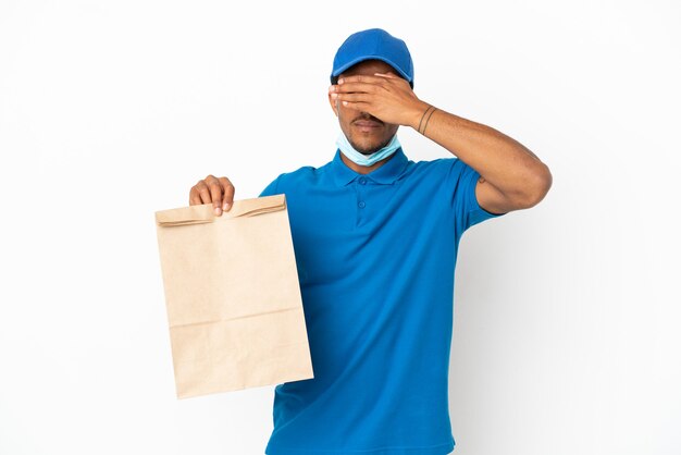 Homem afro-americano, levando uma sacola de comida para viagem, isolada no fundo branco, cobrindo os olhos com as mãos. não quero ver nada