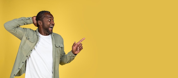 Homem afro-americano maduro feliz chocado em casual com a boca aberta apontando o dedo no espaço vazio